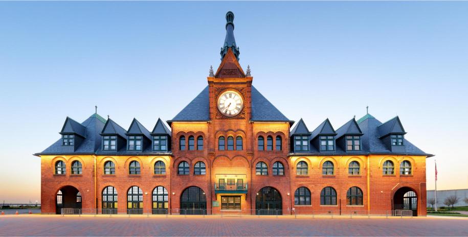 A photograph of a train station with a clock tower, predominantly in a red brick color, with the clock face visible at the top of the tower.