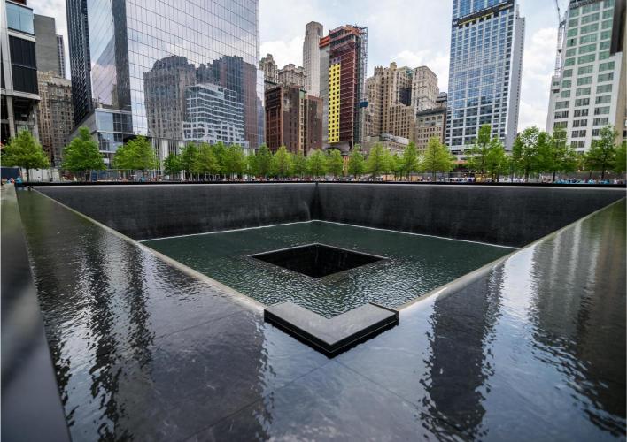 The 9/11 Memorial Reflection Pool with the Manhattan skyline in the background, featuring a clear reflection on the water surface.