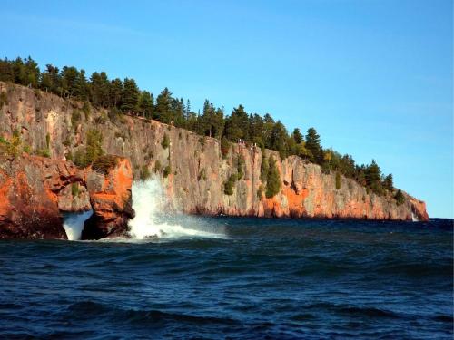 A scenic view of the Lake Superior North Shore with cliffs and a wave crashing against them.