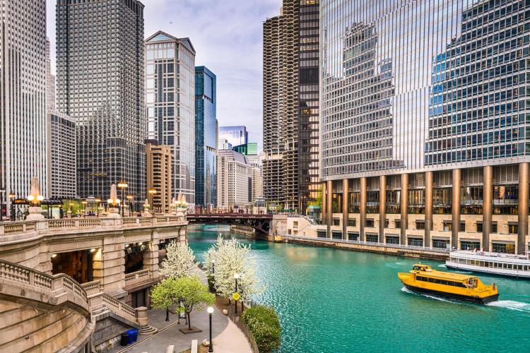 A vibrant image showcasing the skyline of Chicago with a clear view of the Chicago River, featuring a yellow water taxi and surrounding high-rise buildings.