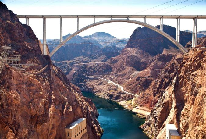 The Hoover Dam Memorial Bridge with an arch design, spanning a river canyon. The bridge is white, and the canyon walls are in shades of brown and blue.