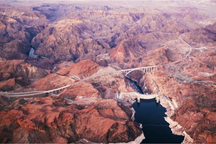 An aerial view of the Hoover Dam and the surrounding landscape, highlighting the Colorado River and the mountains.