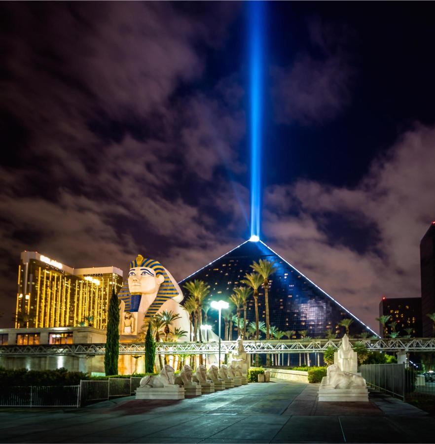 The image shows a night view of the Luxor Hotel in Las Vegas, featuring the hotel's pyramid and a bright light beam extending upwards.