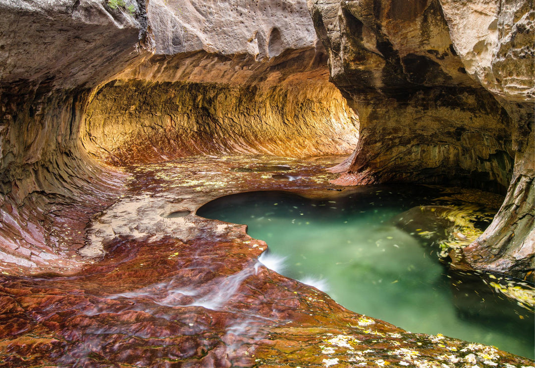 An image depicting a natural archway leading to a pool of water within a cave, with orange, red, and green hues visible in the rock formations.
