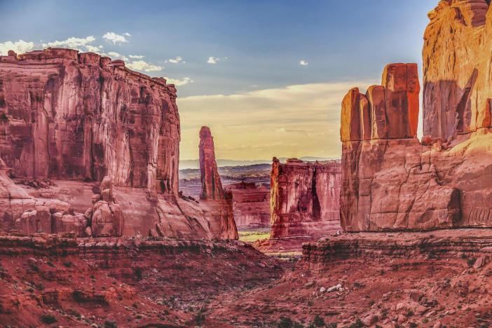 A landscape photograph featuring the sandstone formations of Arches National Park, with warm tones and a clear sky.