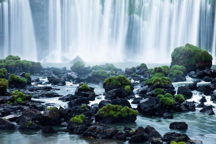 Waterfall with green moss-covered rocks in the foreground.