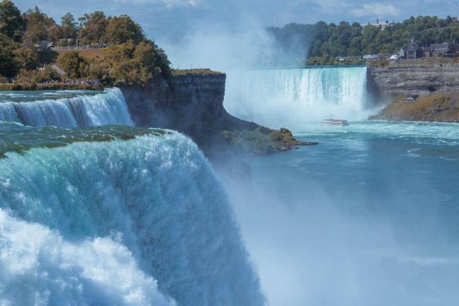 A scenic view of Niagara Falls with water cascading over the edge into a misty river below.