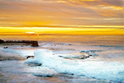 A scenic view of La Jolla Cove with waves crashing and a sunset in the background.