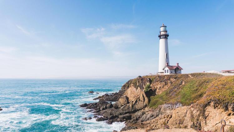 A lighthouse on a cliff overlooking the ocean with a clear blue sky in the background.