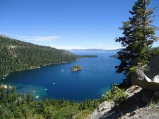 A scenic view of Emerald Bay at Lake Tahoe with clear blue water, surrounded by lush greenery and mountains.