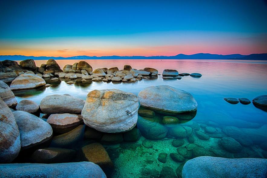 A scenic view of Lake Tahoe featuring a pier, with the lake's clear blue water and a colorful sky at sunset.