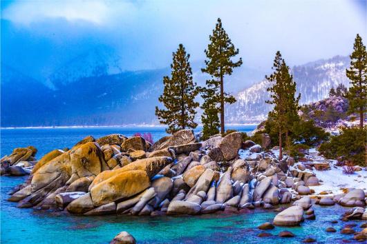 A scenic view of the Lake Tahoe North Shore with trees on a rock formation jutting out of the water, under a blue sky.