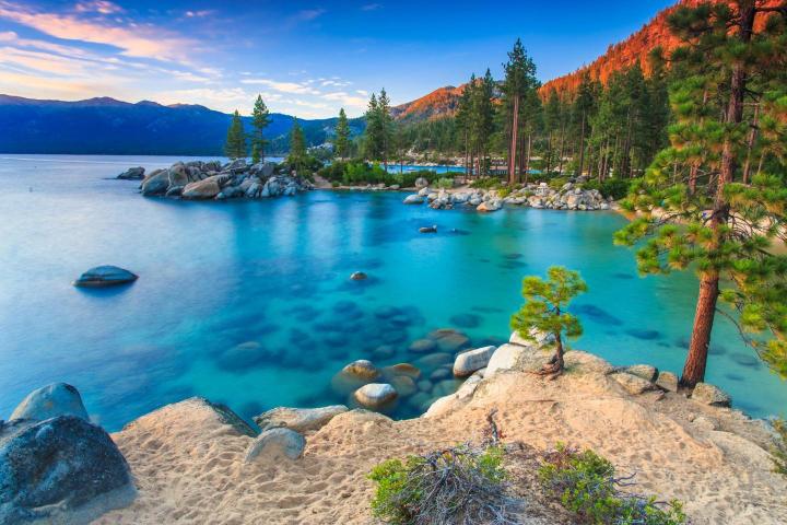 A scenic view of Lake Tahoe Sand Harbor Beach with clear blue water, rocks, and trees.
