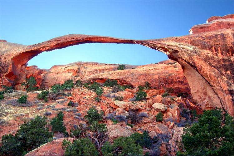 A natural sandstone arch bridge in Arches National Park with red rock formations in the background.