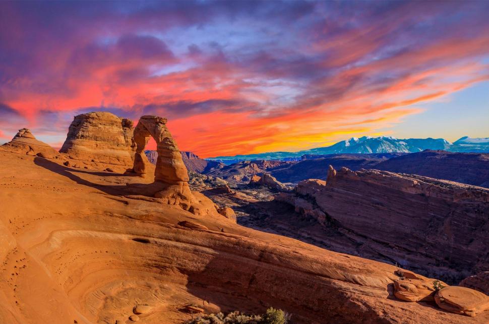 A landscape photograph featuring the Delicate Arch at Arches National Park with a vibrant sunset in the background.