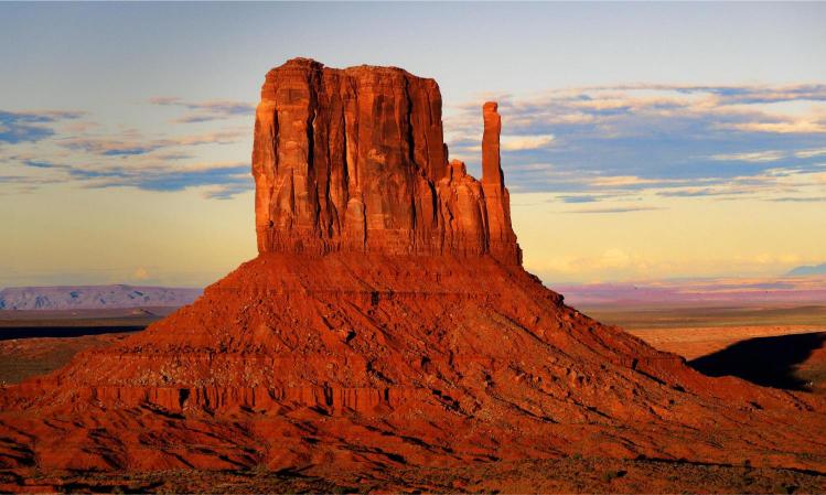 A landscape image of Monument Valley Navajo Tribal Park featuring sandstone buttes under a blue sky with clouds.