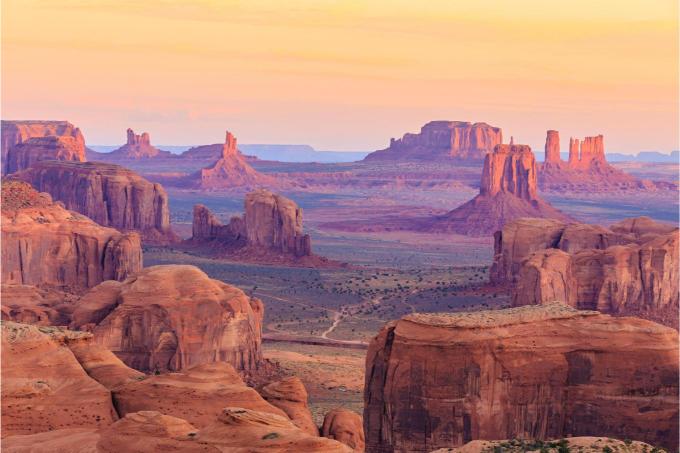 A scenic view of Monument Valley Navajo Tribal Park with sandstone buttes and a pink sky at sunset.