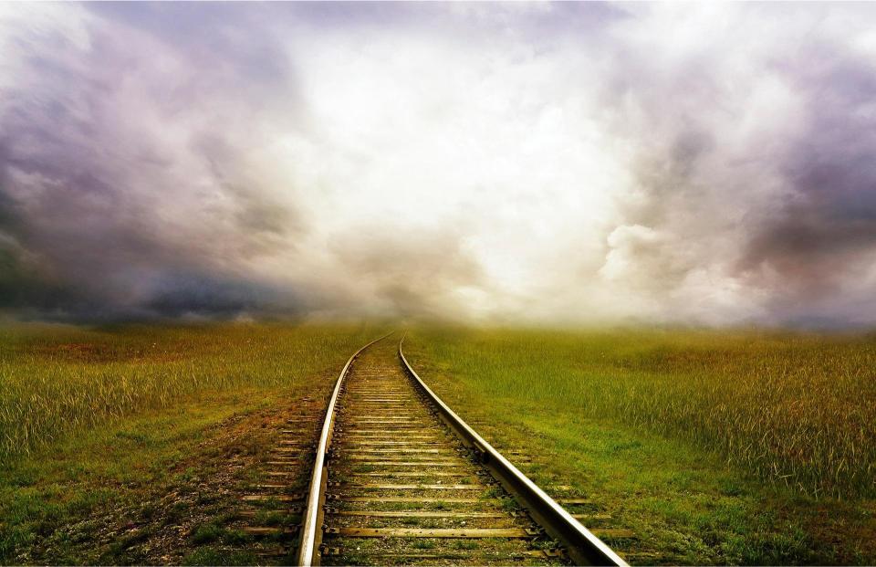 Train tracks leading into a cloudy sky with a grassy field on either side.