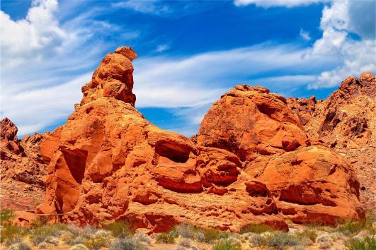 A scenic view of the Valley of Fire with orange and red sandstone formations against a blue sky with clouds.