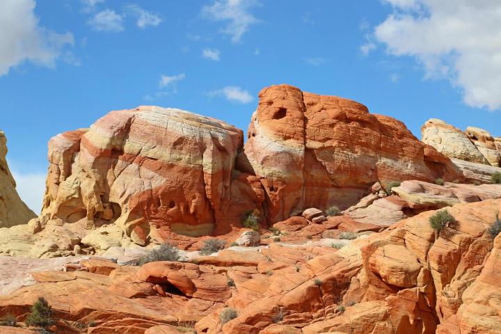 A landscape photo of the Valley of Fire with its characteristic red sandstone formations under a blue sky with some clouds.