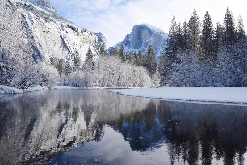 A postcard featuring a scenic view of Yosemite National Park with snow-covered trees and a still body of water reflecting the mountains and sky.