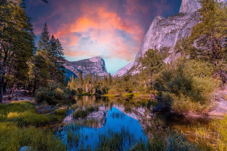 A scenic view of a lake in Yosemite National Park with trees and mountains in the background, reflecting a colorful sky.