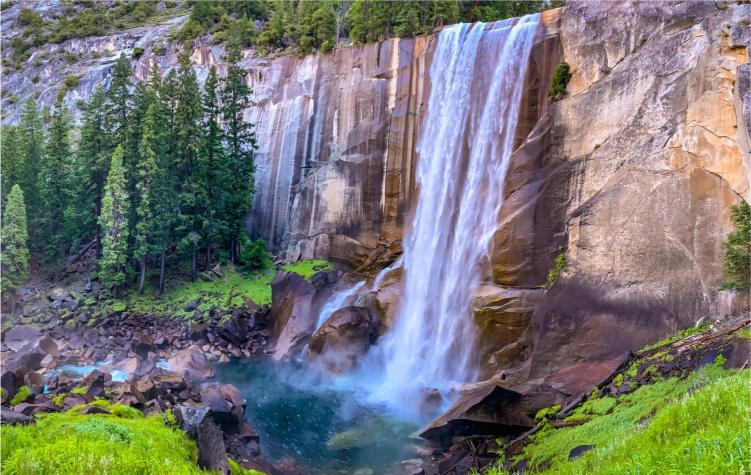 A scenic view of a waterfall in Yosemite National Park, with trees in the background and a clear sky.