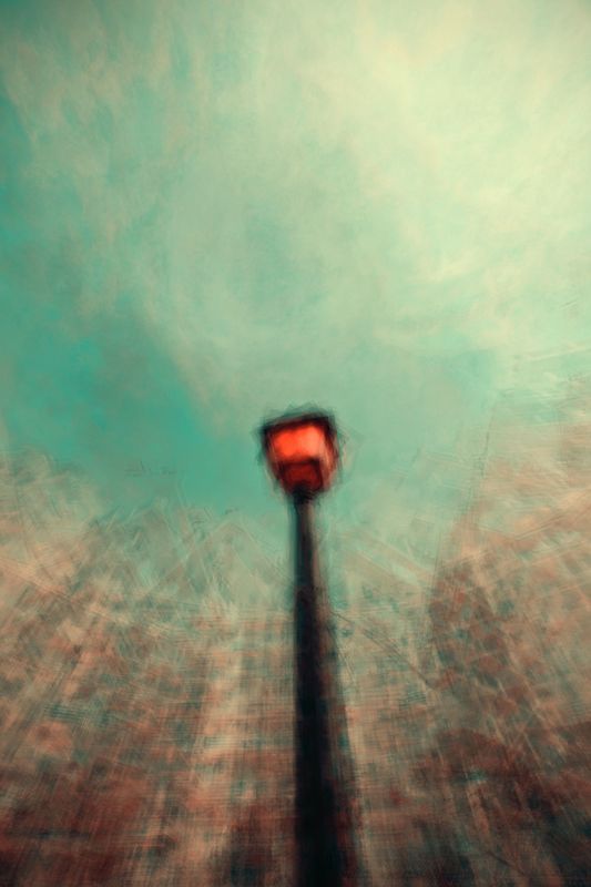 Blurry upward view of a tall black post with a red light against a teal sky, conveying a dreamlike, surreal atmosphere. Edge details are indistinct.