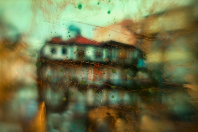 Abstract artwork featuring a building with a red roof and green facade, with a blurred and colorful background.